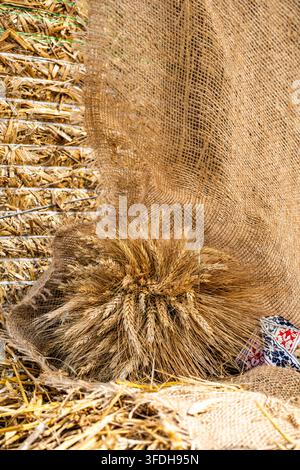 Gros plan vertical d'un bouquet décoratif d'oreilles de blé dorées enveloppées dans une toile de jute rustique sur un fond de paille en plein air. Banque D'Images