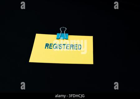 Une note adhésive jaune vif affiche le mot « REGISTERED » estampillé en bleu, sur fond noir profond. Banque D'Images