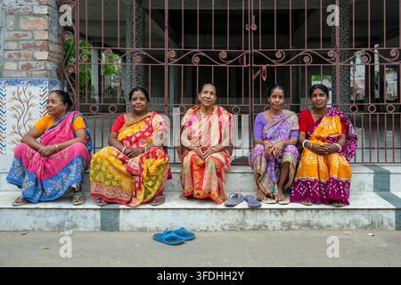 Un groupe de cinq femmes vêtues de vêtements traditionnels indiens vibrants se reposent sur les marches d'un temple ou d'un bâtiment culturel Banque D'Images
