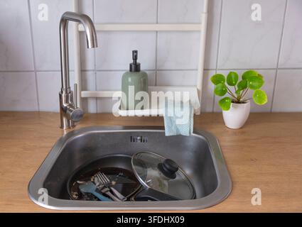 Plat et poêle sales posés dans un évier de cuisine avec de la mousse de savon, représentant le lavage de la vaisselle quotidien et les tâches ménagères. Banque D'Images