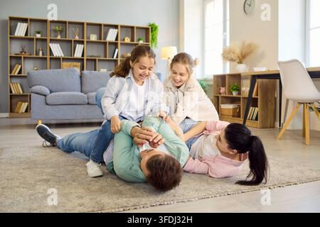Famille heureuse avec parents et filles jouant et se chatouillant sur le sol du salon Banque D'Images