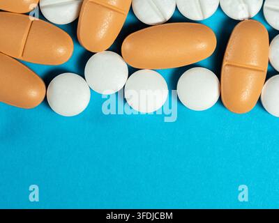 Gros plan de capsules orange et de comprimés ronds blancs éparpillés sur un fond bleu, illustrant les médicaments, le traitement sur ordonnance et la gestion des doses Banque D'Images