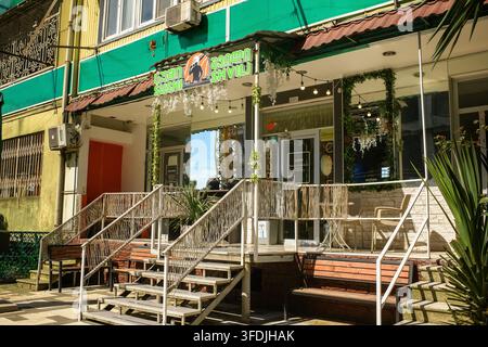 Batumi, Géorgie - 20 mai 2026 : Façade de restaurant avec panneaux publicitaires pour des sushis, escalier d'entrée avec mains courantes, bancs, guirlandes décoratives, livraison de nourriture Banque D'Images