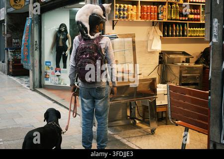 Bogota, Bogota, Colombie – 20 juin 2023 : Vue d'un homme debout dans un magasin avec un chat perché sur ses épaules et un chien noir en laisse à ses côtés. Banque D'Images