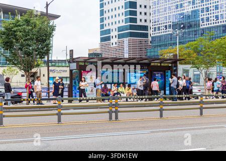 Une grande foule attend à côté d'un abribus urbain et d'une route à plusieurs voies sous des immeubles modernes de grande hauteur à Busan, en Corée du Sud. Banque D'Images