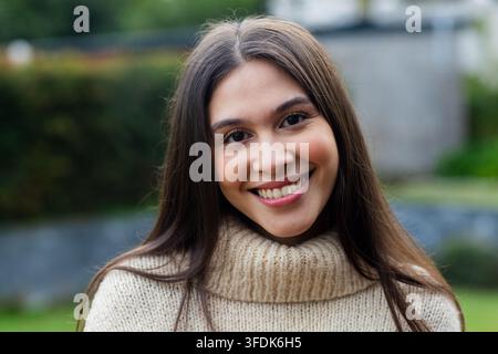Femme souriante posant pour un portrait en gros plan dans un jardin, portant un pull en maille beige à col roulé Banque D'Images
