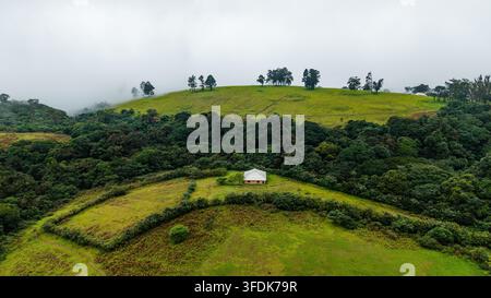 Vue aérienne du Obudu Mountain Resort mettant en scène un petit bâtiment niché parmi des collines vertes luxuriantes, une forêt dense et des prairies ondulantes à Obudu, Cross River Banque D'Images
