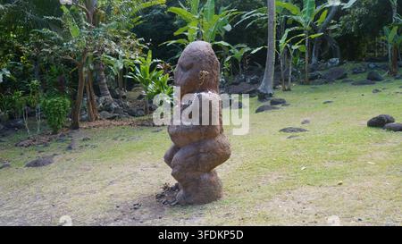 Gros plan d'une ancienne statue de pierre Tiki polynésienne avec un collier de fleurs au Marae Arahurahu à Tahiti Banque D'Images