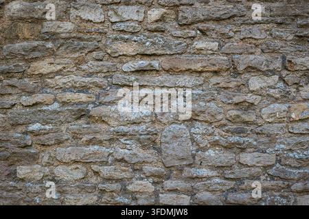 Texture de fond en image complète d'un mur de pierre traditionnel ancien construit avec des roches gris et brun fortement érodées et un mortier rugueux. Banque D'Images