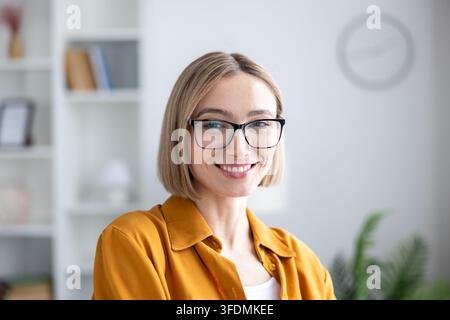 Femme d'affaires confiante souriant largement, portant des lunettes et une chemise décontractée, posant pour un portrait dans un bureau moderne, représentant le succès et le professionnalisme Banque D'Images