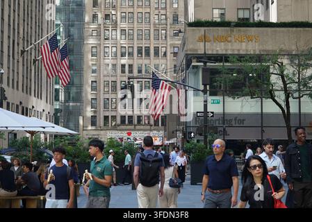 New York, New York, États-Unis : Touristes avec des drapeaux américains à Rockefeller Plaza dans Rockefeller Center, avec les studios NBC News visibles en arrière-plan à M Banque D'Images