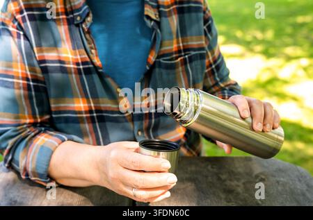 Ancienne femme boit du café dans un thermos lors d'un pique-nique dans le parc. Détendue et profitant de la vie. Journée ensoleillée d'été ou d'automne. Gros plan. Banque D'Images