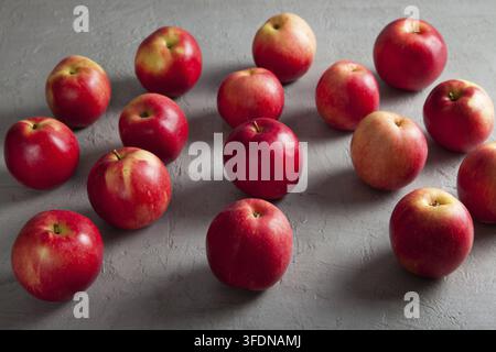 Un groupe de pommes rouges fraîches est éparpillé sur une surface texturée grise, créant une composition alimentaire verticale propre et minimaliste idéale pour les saisons Banque D'Images