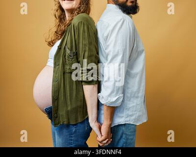 Couple enceinte dos à dos se tenant la main avec une femme enceinte montrant son ventre de maternité Banque D'Images