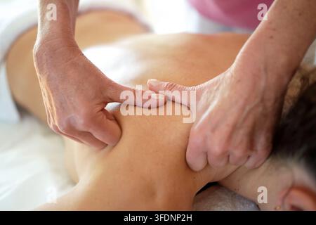 Thérapeute effectuant un massage profond des épaules sur une femme adulte dans une salle de traitement lumineuse avec lumière naturelle, des mains concentrées appliquant une pression de pétrissage Banque D'Images