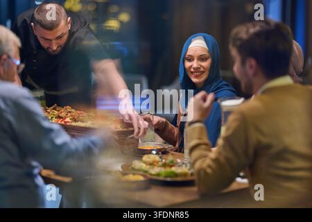 Amis partageant un dîner dans un restaurant avec une femme en hijab souriant alors que le serveur apporte la nourriture Banque D'Images