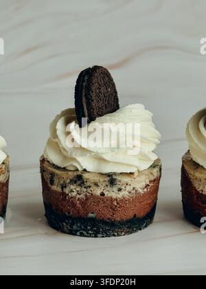 Mini cheesecake au chocolat Oreo garni de crème fouettée et d’un biscuit sur fond de marbre, gros plan Banque D'Images