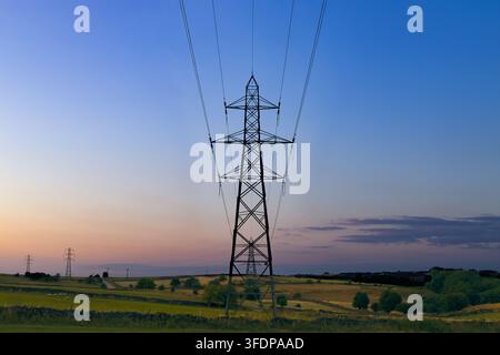 Pylônes électriques transportant des lignes électriques à travers la campagne vallonnée de Brassington, dans le Parc national du Peak District au coucher du soleil, Derbyshire, Angleterre, Royaume-Uni. Banque D'Images