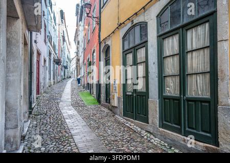 Rue pavée étroite serpente à travers un quartier historique portugais bordé de bâtiments colorés, de hautes fenêtres et de portes en bois vert, évoque Banque D'Images