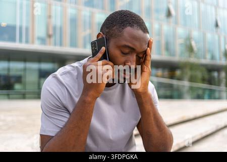 Triste fatigué solitaire homme africain déçu seul parlant sur smartphone sur la rue de la ville en plein air. Personne malheureuse faisant répondre à l'appel par téléphone portable éprouvant le chagrin obtenir de mauvaises nouvelles. Homme stressé Banque D'Images