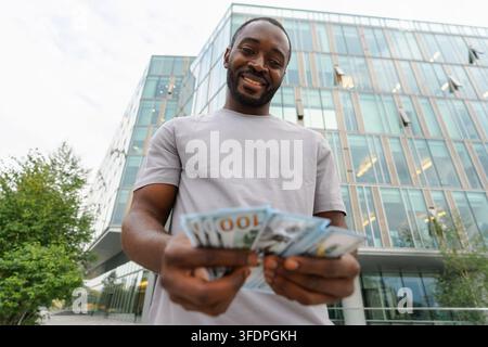Homme afro-américain tenant des billets d'argent en dollars dans la rue urbaine en ville. Homme d'affaires comptant l'argent de papier monnaie à l'extérieur près de l'immeuble de la banque de bureau. Homme tenant de l'argent. Finance Economy Banking Banque D'Images