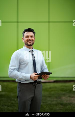 Homme confiant tenant une tablette debout contre un mur vert Banque D'Images