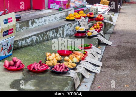 Des pêches variées, des poires, des oignons, des pommes de terre, des patates douces, des poivrons et des carottes sont disposés dans des bols et des boîtes sur les marches en béton du marché. Banque D'Images