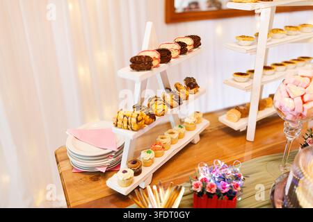 Présentation élégante de desserts comprenant des rangées de mini cupcakes variés, des pâtisseries au chocolat, des biscuits et d'autres douceurs disposées sur des plateaux blancs à plusieurs niveaux Banque D'Images