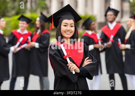 Jeune étudiante asiatique heureuse célébrant une fête de fin d'études, portant un costume de graduation et tenant un diplôme, jolie diplômée posant fièrement à l'université Banque D'Images