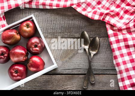Pommes rouges bien mûrs en bouleau-box sur planche de bois avec une serviette autour de rouge à carreaux, et les cuillères et copie de l'espace pour votre recette. Banque D'Images