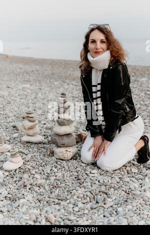 Femme de plage, femme zen agenouillée sur un rivage de galets près de piles de pierres équilibrées pour la pleine conscience Banque D'Images