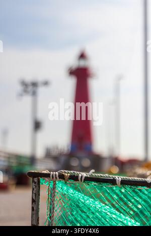 Grossissement d'un filet de pêche vert et d'une corde fixés à un cadre métallique usé sur un fond flou de bord de mer. Banque D'Images