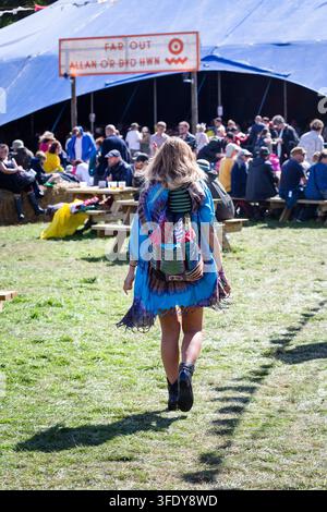 FESTIVALIER EN STYLE HIPPIE TRAVERSE UN CHAMP, REPORTAGE, GREEN MAN FESTIVAL 2017, BRECON, WALES, UK, 2017 : Vu de dos, une jeune femme avec un sac à dos coloré et un haut tie-dye traverse un champ herbeux en direction de la grande tente bleue Far Out lors d'un festival. Photo : Rob Watkins. INFO : Le Green Man Festival a débuté en 2003 au Pays de Galles. Organisé chaque année dans les Brecon Beacons le troisième week-end d'août, il célèbre la musique alternative, les arts, la littérature, la science et une culture familiale dans un magnifique cadre montagneux. Banque D'Images