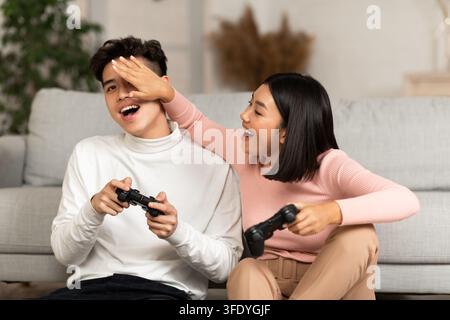 Joyeux ami coréen et petite amie jouant aux jeux vidéo à la maison Banque D'Images