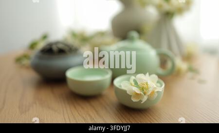 Configuration traditionnelle pour une cérémonie du thé avec une théière verte, des tasses à thé, des feuilles de thé sèches et des fleurs de jasmin blanches. Banque D'Images