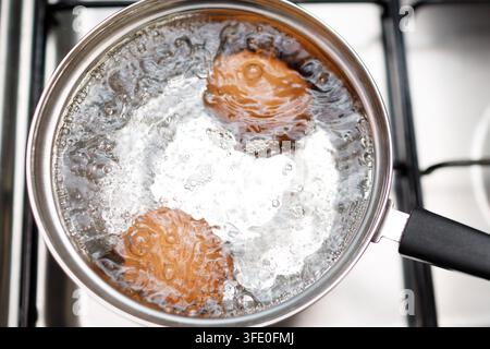 Casserole en acier inoxydable avec des œufs bouillants petit déjeuner dans une eau sur une cuisinière à gaz Banque D'Images