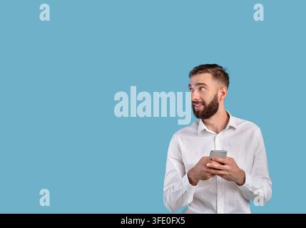 Un jeune homme d'affaires heureux avec un téléphone portable qui cherche un espace vide sur fond de studio bleu Banque D'Images