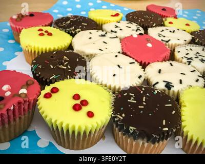 Une collection méticuleusement stylée de mini cupcakes gastronomiques avec un glaçage jaune vif, rose et riche au chocolat, ornés de paillettes délicates, pr Banque D'Images