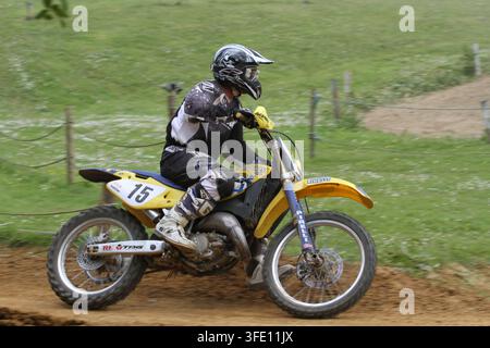 Un pilote de motocross sur une moto tout-terrain Suzuki jaune numéro 15 filant sur une piste en terre lors d'une compétition de sport automobile tout-terrain. Banque D'Images