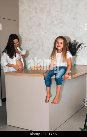 Mère enceinte et fille heureuse passant du temps ensemble dans une cuisine moderne Banque D'Images