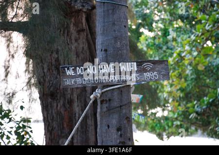 Panneau en bois rustique sur un bar de plage portant l'inscription "Nous n'avons pas de WiFi, parlez-vous les uns aux autres, faites comme si c'était 1995" monté sur un tronc d'arbre. Banque D'Images