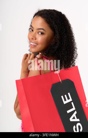 Une jeune femme afro-américaine sourit joyeusement en faisant ses courses, mettant en valeur son sac de solde vibrant. Banque D'Images