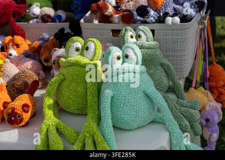Vue rapprochée de grenouilles en peluche amigurumi tricotées à la main, exposées sur une table d'un marché artisanal en plein air. La collection d'artisanat présente du chenille doux Banque D'Images