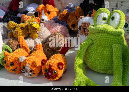 Vue rapprochée d'une grande grenouille en peluche verte crochetée assise à côté d'une variété d'animaux amigurumi fabriqués à la main sur une table d'exposition en plein air Banque D'Images