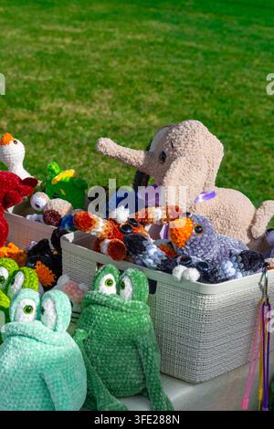 Vue rapprochée de jouets en peluche Amigurumi crochetés à la main exposés dans des paniers de rangement blancs sur un marché artisanal en plein air. La collection d'artisans met en vedette Banque D'Images