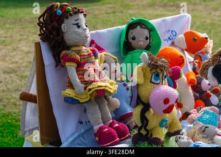 Vue rapprochée d'une collection de poupées Amigurumi crochetées à la main et de peluches exposées sur un tissu blanc dans un marché artisanal en plein air, feat Banque D'Images