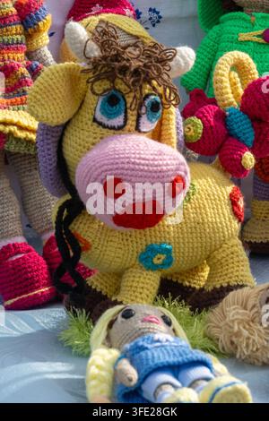 Vue rapprochée d'un jouet amigurumi tricoté à la main en forme de vache jaune joyeuse avec un museau rose proéminent, des yeux bleus et des cheveux bouclés bruns, exposé alo Banque D'Images