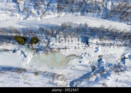 Vue aérienne d'une rivière partiellement gelée serpentant à travers un paysage forestier enneigé avec des arbres à feuilles persistantes et de profondes congères à Valldal, More og R Banque D'Images