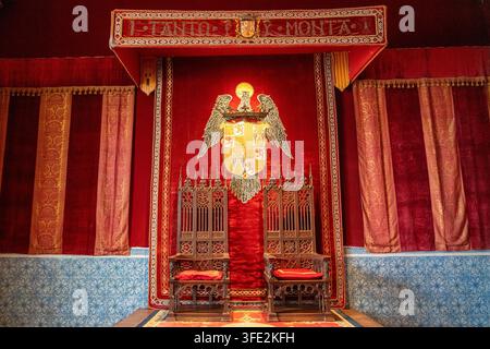 Salle du trône somptueuse en velours rouge avec deux chaises en bois sculptées, un blason doré et des draperies ornées à l'Alcázar de Ségovie, Espagne — un historique Banque D'Images