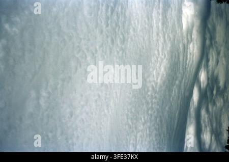 Extrême gros plan d'une cascade massive révélant une eau blanche tumultueuse et dévalante avec des motifs d'écume tourbillonnants, créant une texture abstraite puissante. Banque D'Images